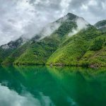 Koman Lake surrounded by majestic mountains and white clouds in the sky.