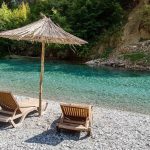 Two sunbeds with an artisanal umbrella on the tranquil shore of Shala River, perfect for relaxation.