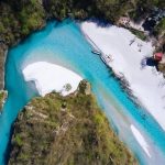 op view of Shala River with crystal-clear blue water surrounded by lush greenery.