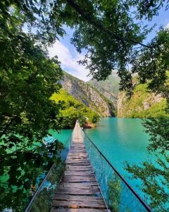 Wooden bridge crossing over the crystal-clear waters of Shala River surrounded by lush greenery.