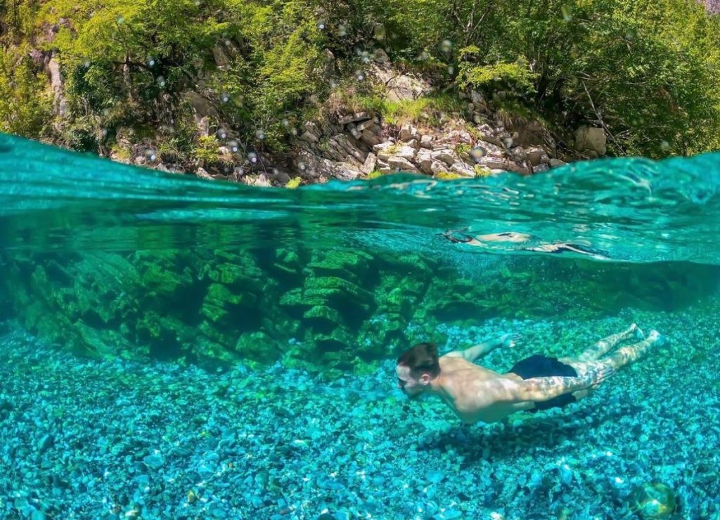 Tourist diving into the crystal-clear waters of Shala River, surrounded by mountains.