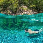 Tourist diving into the crystal-clear waters of Shala River, surrounded by mountains.