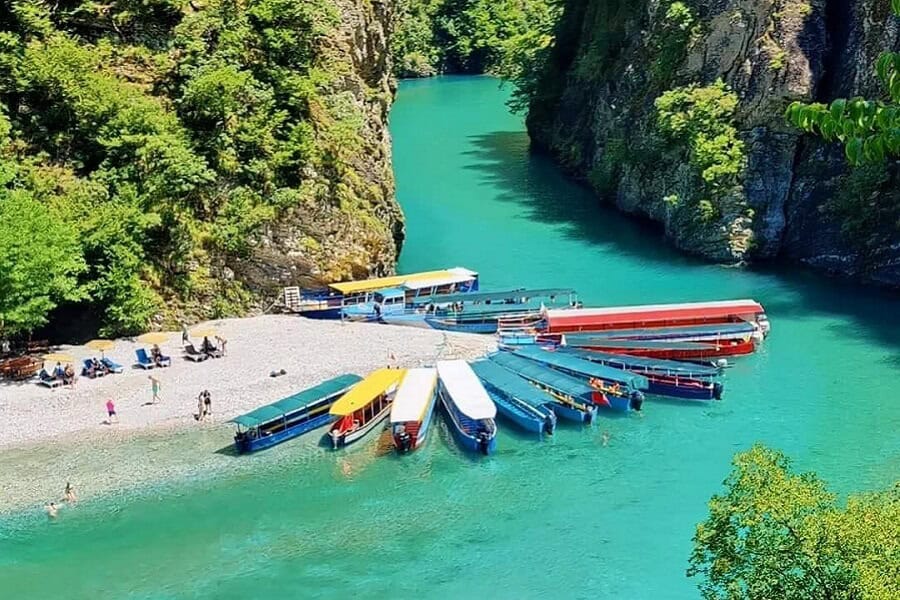 Aerial view of how to visit Shala River with excursion boats on Shala River's white pebble beach with turquoise water and canyon walls