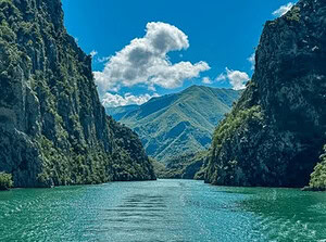 Näkymä veneestä Komani-järvellä, katsellen kapean kanjonin läpi turkoosinvihreällä vedellä ja vuorenhuipuilla taustalla, Pohjois-Albaniassa