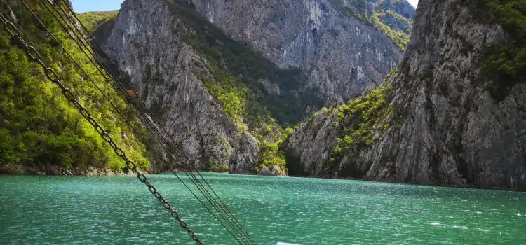 Widok z pokładu łodzi nad jeziorem Komani przez wąski wąwóz z zieloną wodą i pionowymi skalnymi ścianami po obu stronach, Albania
