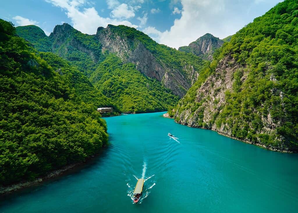 Widok z powietrza na dwa statki przecinające żywe turkusowe wody Jeziora Komani otoczone stromymi, porośniętymi lasem górami na północy Albanii.