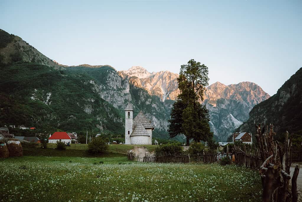 Theth church Albania evening light wildflower meadow traditional stone building Albanian Alps mountains northern Albania