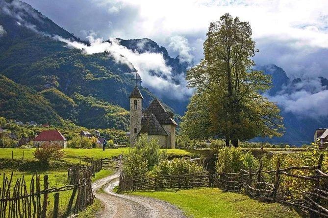 Theth church Albania misty morning low clouds traditional stone building Albanian Alps mountains atmosphere