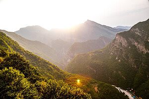 Golden sunset over a wide forested mountain valley in the Albanian Alps with the Drin River and small settlement visible far below, seen on the drive from Lezhe to Komani Lake on the Shala River day tour