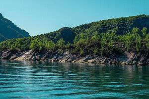 Peaceful Komani Lake shoreline with green mountains on the Lezhe to Shala River boat tour in northern Albania