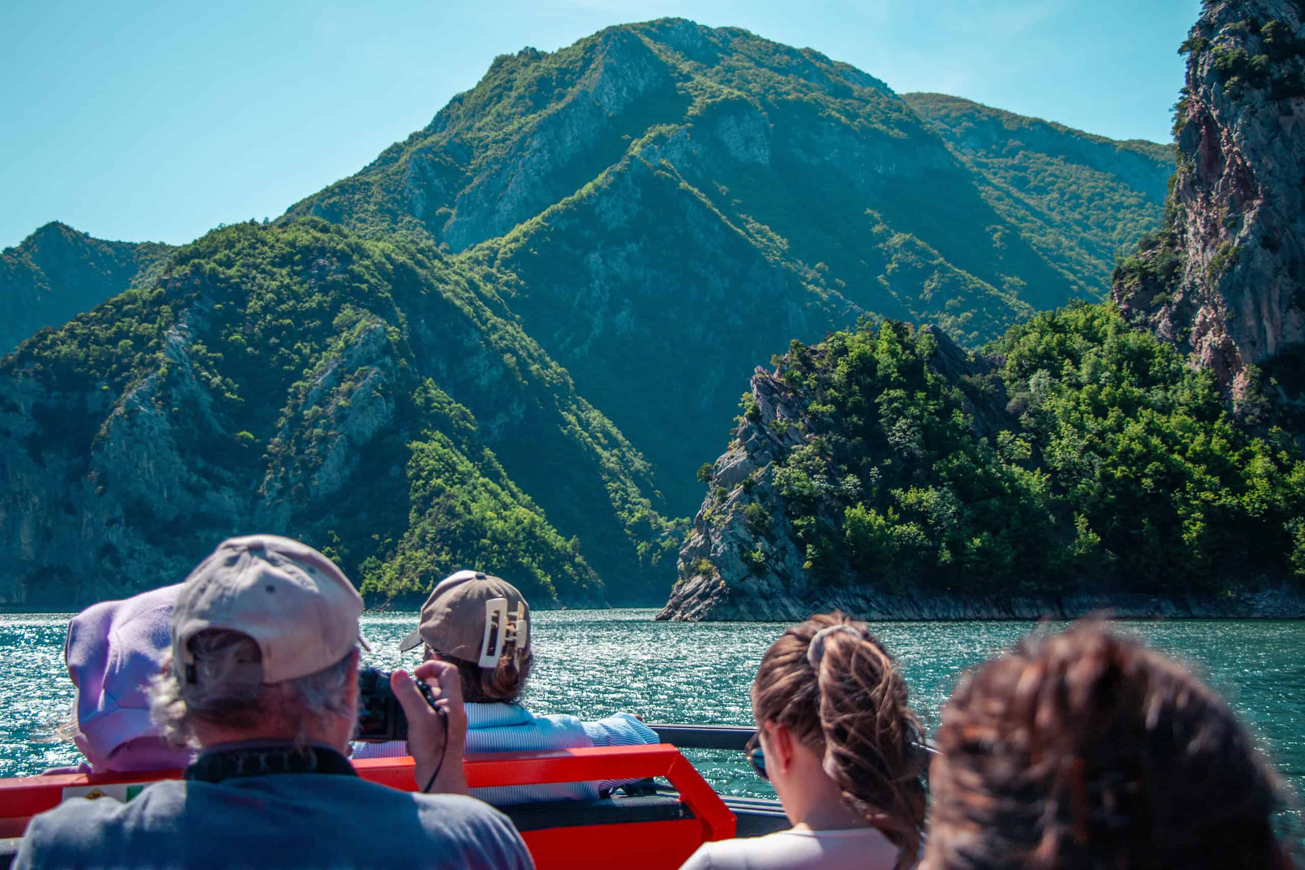 Group of tourists on the open deck of a tour boat photographing the narrow gorge entrance on Komani Lake as the boat heads toward Shala River, northern Albania