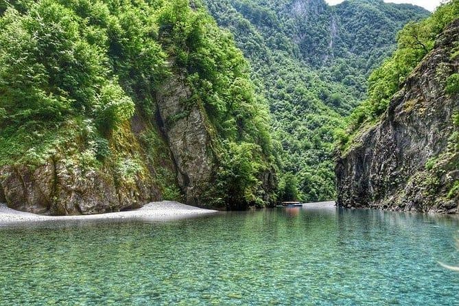 Small boat in the crystal clear turquoise water of the Shala River inner canyon with limestone cliffs and forest, northern Albania