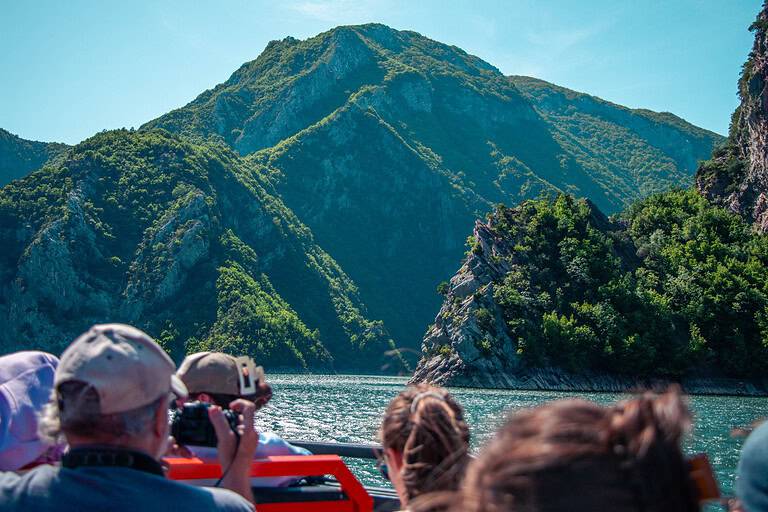 Tourists seated on the open deck of a North Albania Boat modern boat photographing the dramatic rocky canyon and turquoise water of Komani Lake, Albania
