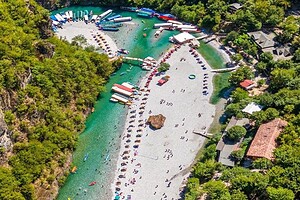 Aerial drone view of Shala River pebble beach crowded with boats, sunbeds and visitors during peak summer season in Albania