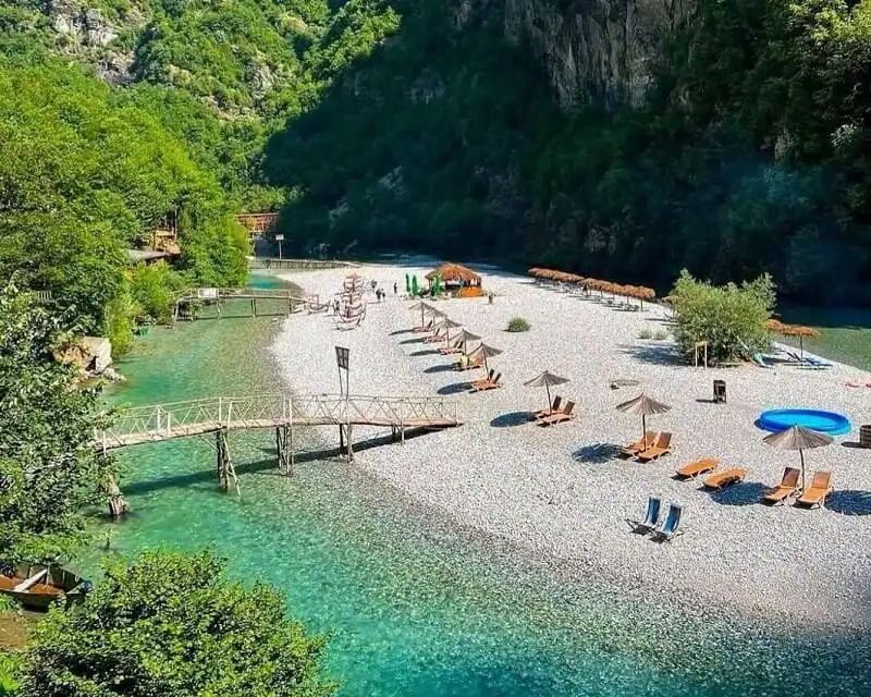 Shala River beach with wooden footbridge, sun loungers, thatched parasols and canyon forest, northern Albania boat tour