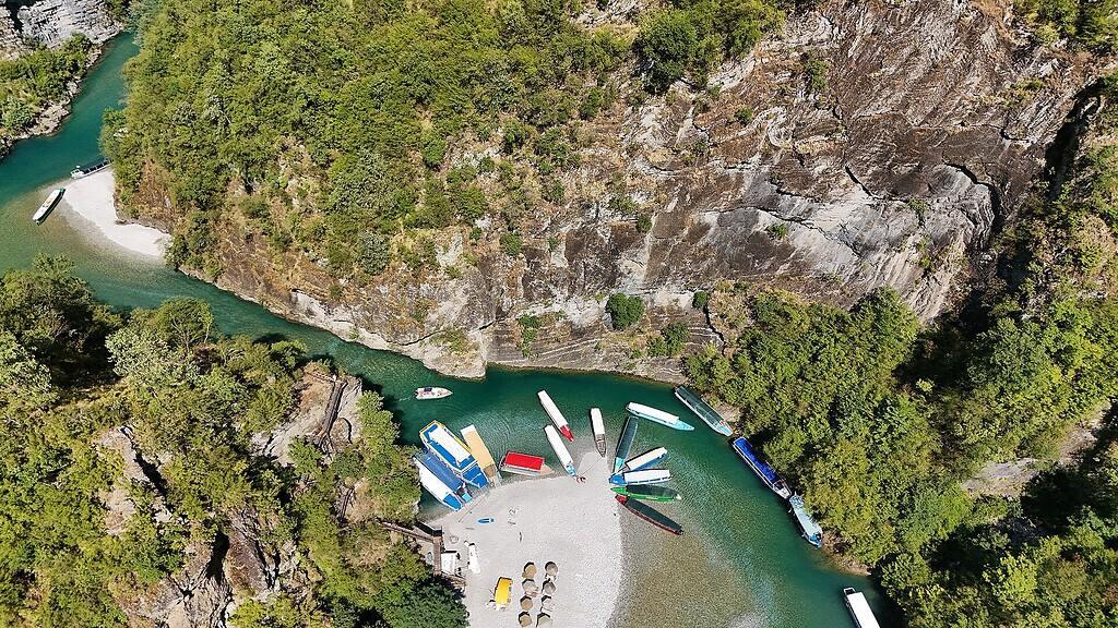 Drone view of boats docking at Shala River beach surrounded by mountains in northern Albania
