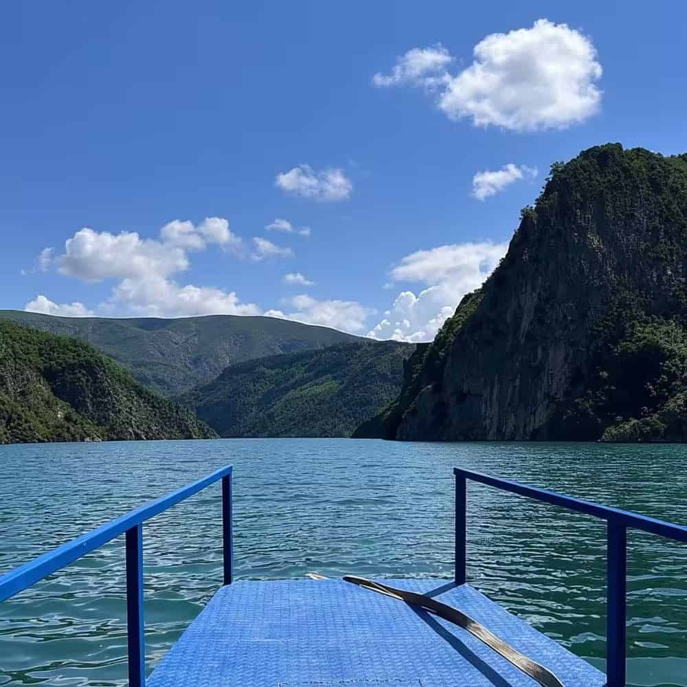 View from boat on a day trip from Tirana railing over turquoise Komani Lake surrounded by green mountains