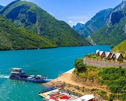 Ferry boat and wooden lodges on the turquoise shore of Komani Lake