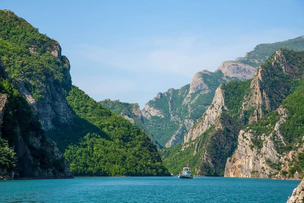 Ferry boat sailing through narrow green canyon on Komani Lake