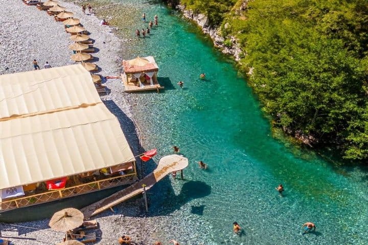 Aerial view of Shala River beach club with umbrellas and swimmers in turquoise water