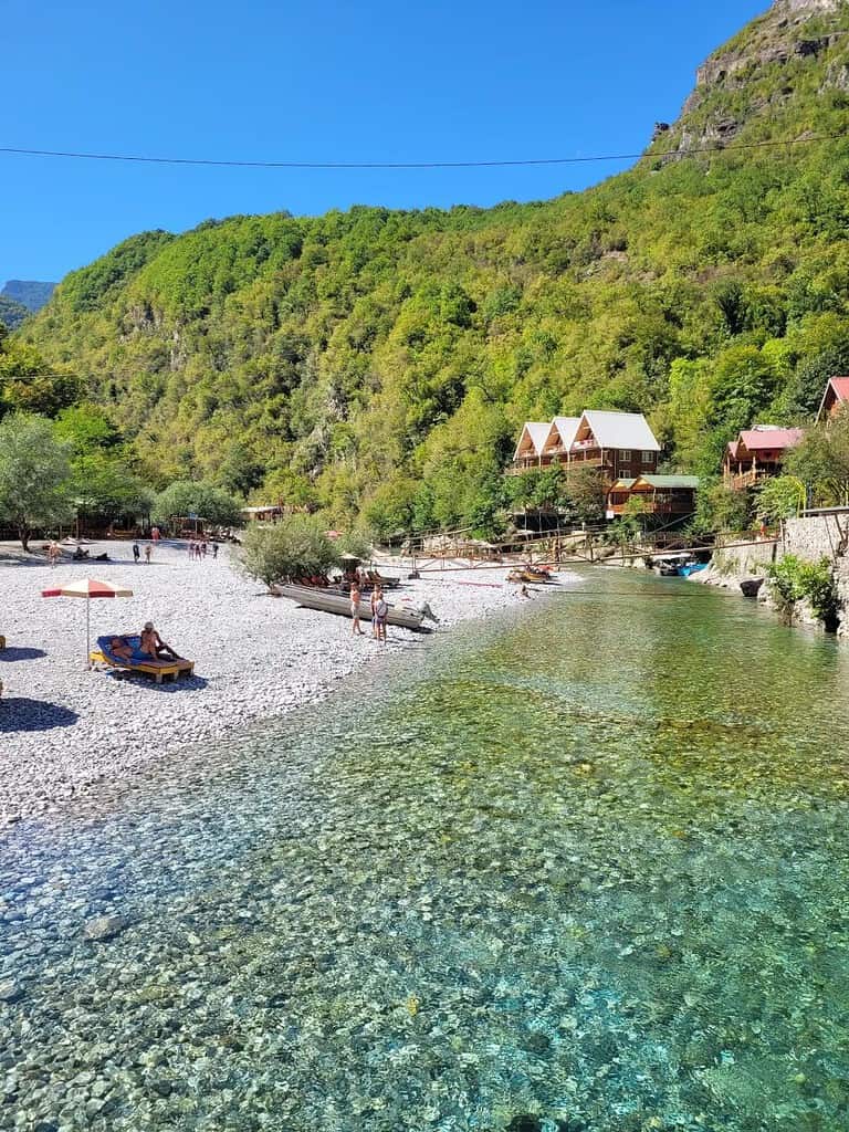 Pebble beach at Shala River with wooden guesthouses and kayaks, Albania