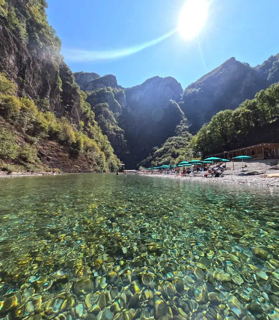 Sunny shoreline at Shala River with umbrellas and swimmers, Albania