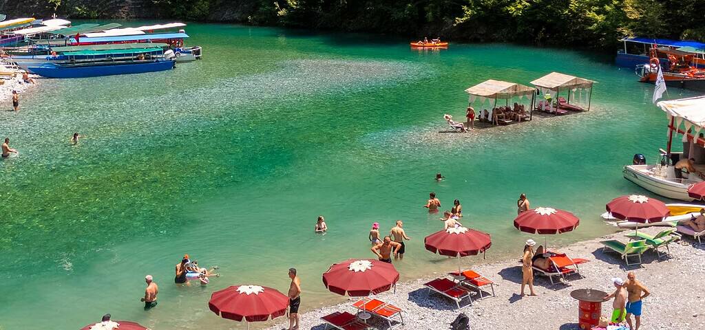 Boats moored beside the main swimming area at Shala River with umbrellas on the beach, Albania