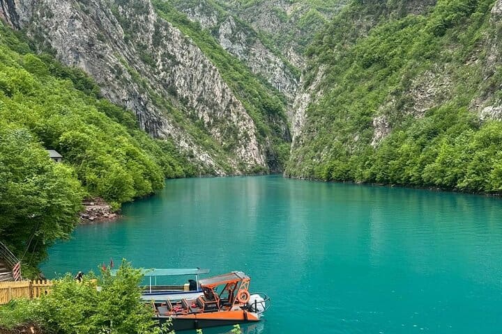 Passenger boat on turquoise Komani Lake between steep forested mountains in Albania