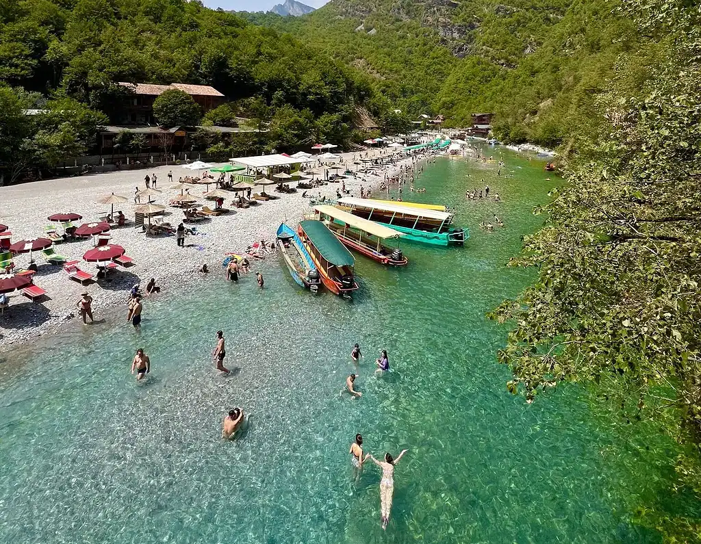Visitors swimming at Shala River beach with tour boats on clear turquoise water