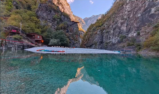 Still turquoise water at Shala River reflecting the canyon cliffs, with a cabin and kayaks on the beach