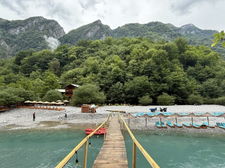 Wooden pier with yellow railings leading to sunbeds and umbrellas on the Shala River pebble beach