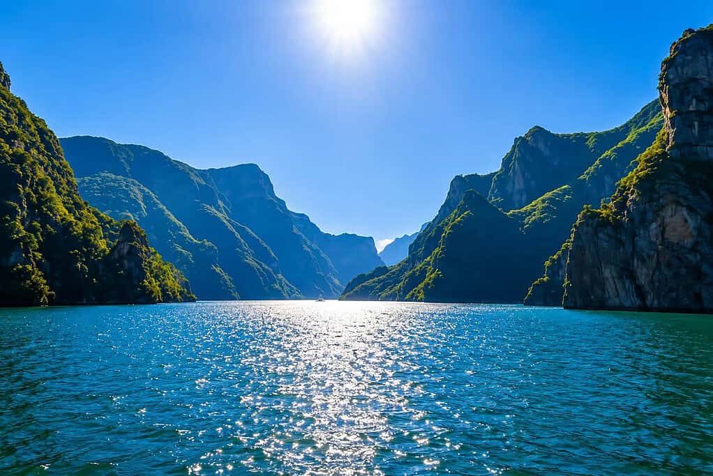 Sun reflecting on Komani Lake between steep green cliffs, seen from water level in northern Albania