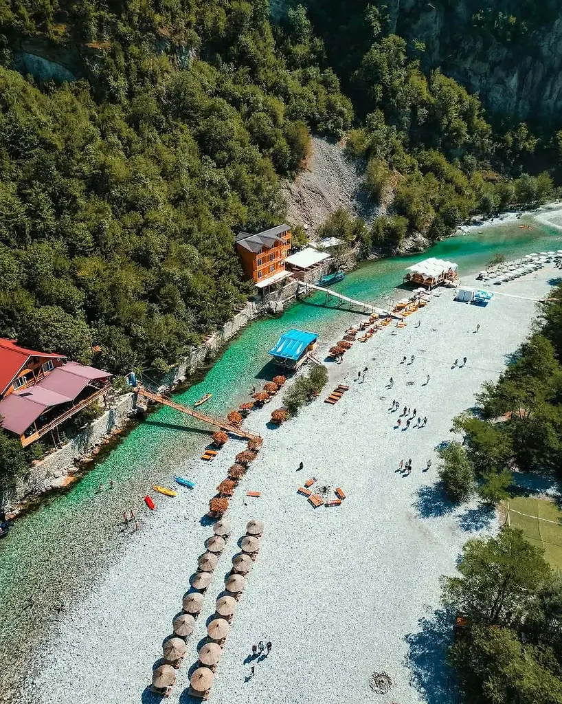 Aerial view of the Shala River's turquoise water, pebble beach and umbrellas in a forested canyon