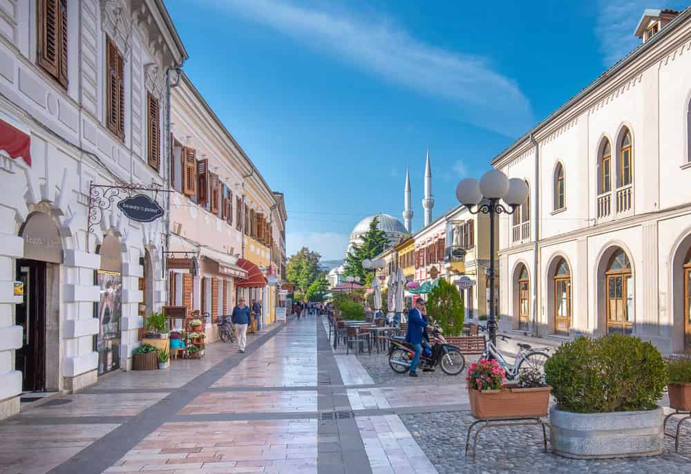 Historic pedestrian street in Shkoder with cafes, flower pots and a mosque dome and minarets in the distance