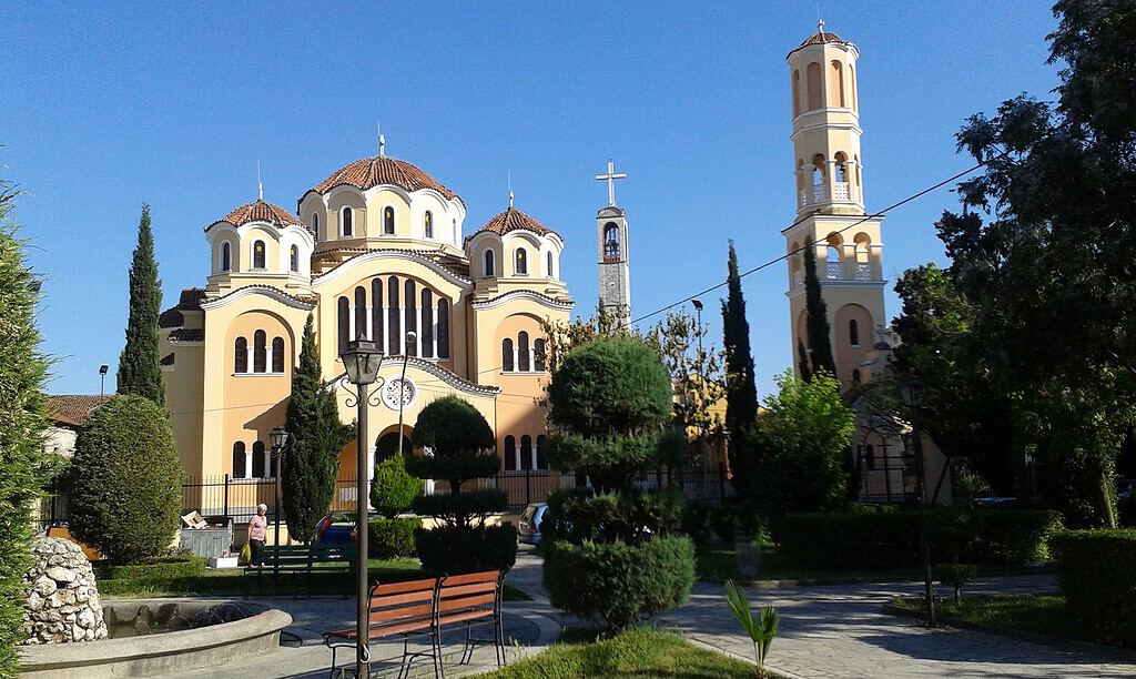 Yellow Orthodox cathedral with three domes and two bell towers in a garden with cypress trees in Shkoder